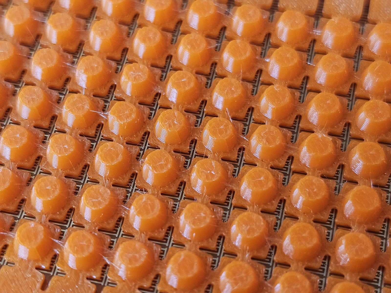 Close-up of a printed bump sheet seated on a flex PCB: each bump's cross-shaped base sits in the gaps between the gold taxel electrodes.