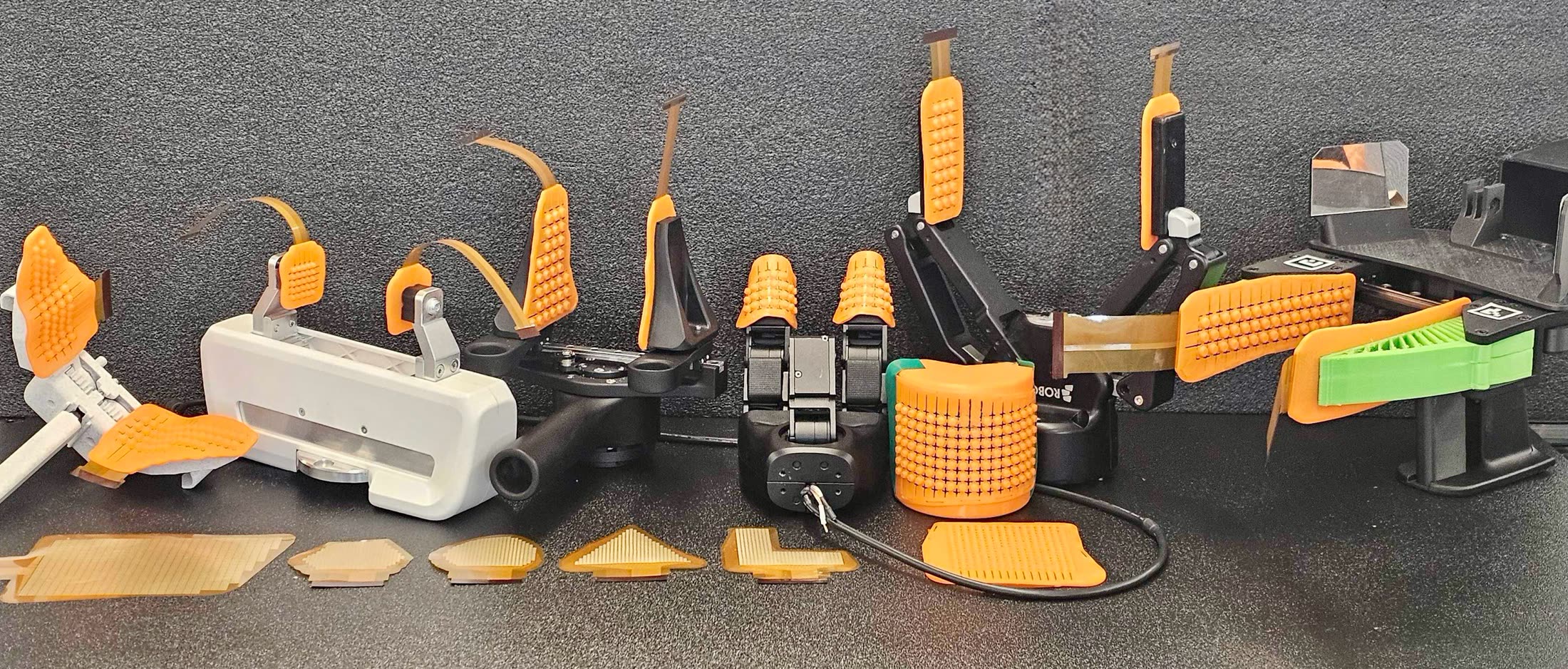 OpenTac skins on robot parts: orange bump sheets over flex PCBs on gripper fingers, a fingertip, a foot and a curved pad, with bare flex PCBs in front.